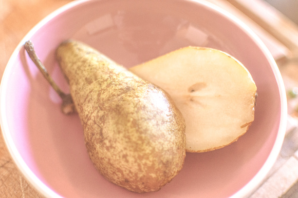 A deliciously look pear cut in half presented on a pink plate